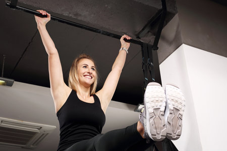 Pull-ups on the stick. Sports training, a young attractive woman does exercises in the gym club.の写真素材