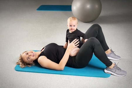 Training with a baby. A woman trains with a child in a fitness room.の写真素材