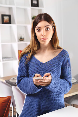 Woman with the phone. Addiction to the phone. A woman with a cell phone is standing in the living room.の写真素材