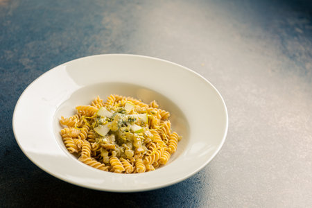 High angle view of wholegrain pasta with slices of pear and gorgonzola cheese in big round plate on dark tableの写真素材