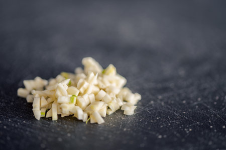Detail of small cut garlic lying on black kitchen black board with blurred backgroundの写真素材