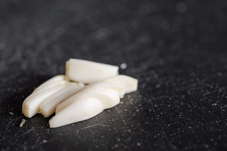 Detail of small cut garlic lying on black kitchen black board with blurred background