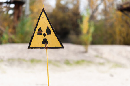 Yellow radioactive warning sign on metal rod in Chernobyl Exclusion Zone of Alienation with blurred...