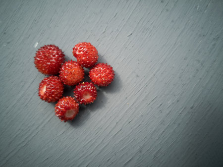 Close up of  a small batch of seven red wild strawberries lying on grey table, ripe and ready to eatの写真素材