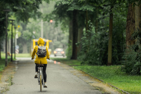 One unrecognizable person with yellow oilskin on bike riding through rainy street in beautiful old alley with trees on rainy dayの写真素材
