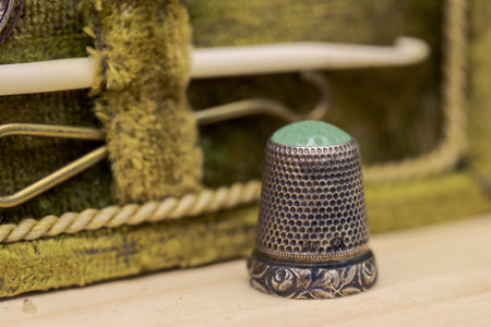 Antique thimble made of iron and green glaas standing on wooden board with old sewing kit in blurred backgroundの写真素材