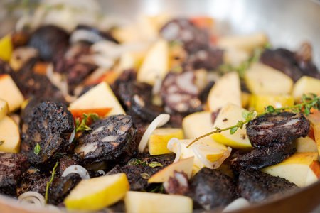 Full frame slices of blood sausage and apples mixed with onions and herbs like thyme sizzling in...