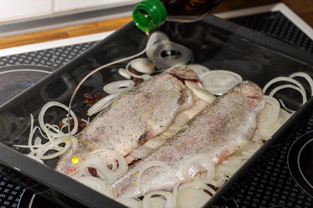 Pouring olive oil over two raw trouts stuffed with herbs, onions and raisins lying in deep frying panの写真素材