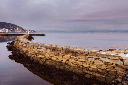 Quay wall with lighthouse of the Trondheim port on overcast winter dayの写真素材