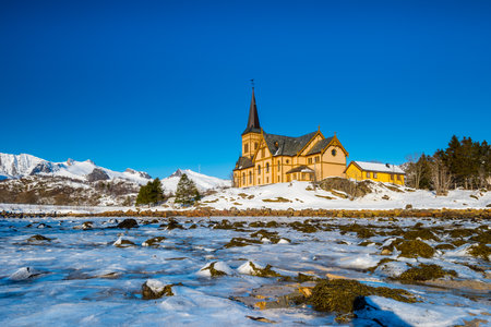 The wooden yellow VÃ¥gan Church on the beach on the Lofoten islands in Norway in winter with frozen river and mountains in morning lightの写真素材