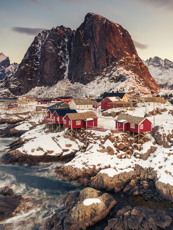 Iconic red stilt houses on the coast in the village HamnÃ¸y on the Lofoten islands in Norway on clear winter morning with snow-clad steep mountainの写真素材