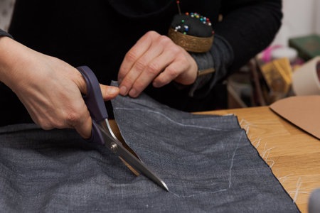 Human hands cutting out the template of fabric with dressmaker shear for making protective face masks at home during lockdown of Covid crisisの写真素材