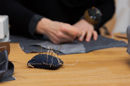 Workplace of needlewoman on wooden table with pincushion and fabric with out of focus human hands in backgroundの写真素材