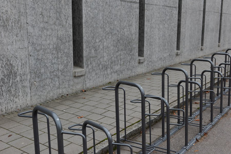 Long row of empty bike racks next to sidewalk near closed public school with bleak gray conrete wall...