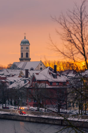 The tower of the church St. Mang in Regensburg on the danube river on cold winter morning in December with fresh snow on the roofsの写真素材