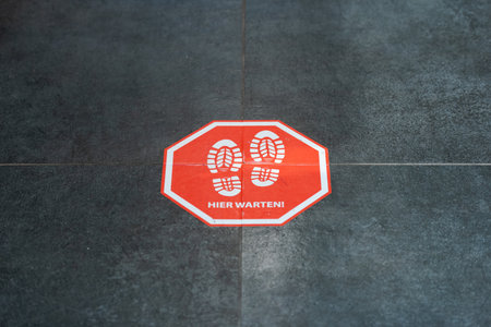 Munich, Germany - 2021 02 05: Stop sign on floor in german organic supermarket with german words for please waitのeditorial素材