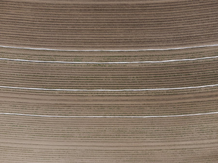 Aerial view down on empty barren field with very dry soil and plow furrows in bright sun light