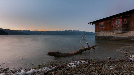 Idyllic calm soothing morning scenery at mountain lake Walchensee in Bavaria, Germany at dawn with boat house and dead tree branchの写真素材