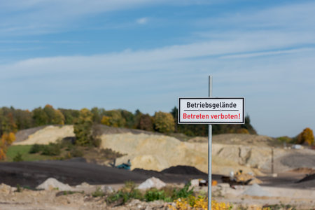 Regensburg, Germany - 2021 10 20: Warning sign on metal post with german text Betriebsgelande betreten verboten meaning factory premises no trespassing standing at quarry with machines and quarry in blurred backgroundstone pitのeditorial素材