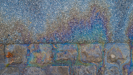 Shimmery and shiny trail and puddle of oil, gasoline or diesel on the side of paved roadの写真素材