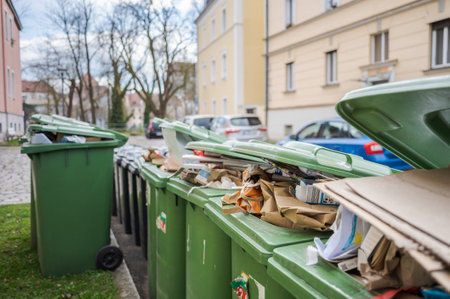 Row of brimful municipal paper bank waste trash cans with open lids for cardboard standing on open street in residential urban areaの写真素材