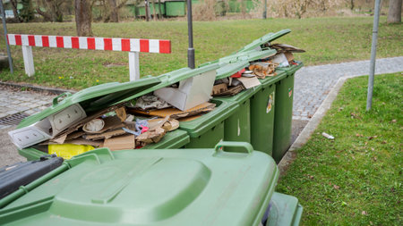 Row of brimful municipal paper bank waste trash cans with open lids for cardboard standing on open street in residential urban areaの写真素材