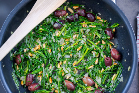 The salty vegetable agretti, friarÂ´s beard, in pan on oven with onions, pine nuts and olivesの写真素材