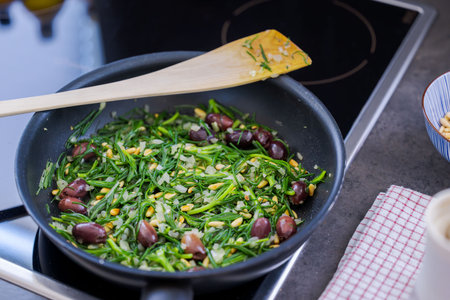 The salty vegetable agretti, friarÂ´s beard, in pan on oven with onions, pine nuts and olivesの写真素材