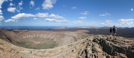 Two hikers walk on the crater rim of Caldera Blanca, one of the largest volcanic crater in Lanzarote, Canary Islands, Spain.のeditorial素材