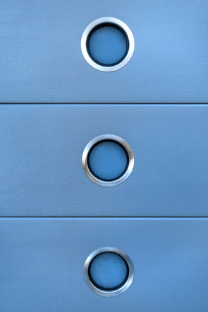 Detail of a design with a light blue, textured surface and three silver bordered, small portholes