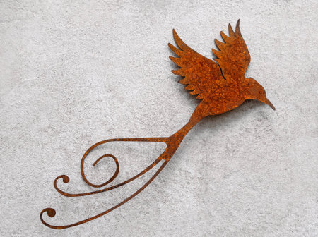 Handcrafted, flying bird made of metal with an artistically designed tail on a white-gray exterior wallの写真素材