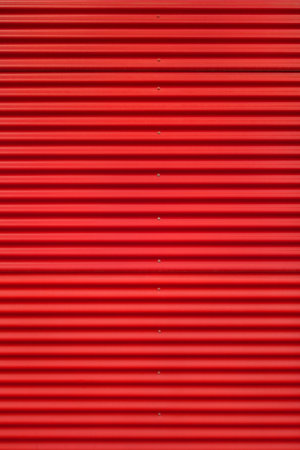 Detail shot of a red corrugated iron with horizontal pattern and one vertical row of silver screws on to exterior wall.の写真素材