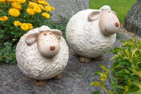 Two funny, small, thick, smiling, white, stained and so Partially damaged sheep made of ceramic Stood in a front gardenの写真素材