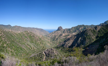 The elongated valley of Vallehermoso, La Gomera, Canary Islands, Spain, northbound. In the middle the distinctive rock summit Roque El Cano. The elongated valley of Vallehermoso, La Gomera, Canary Islands, Spain, northbound. In the middle the distinctive rock summit Roque El Cano.