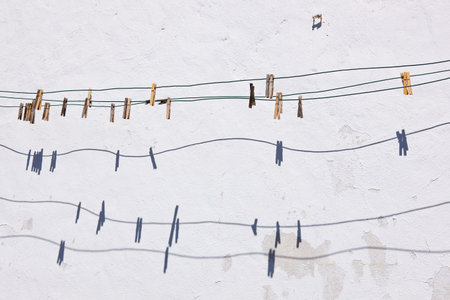Wooden clothespins on the clothesline cast shadows on a weathered white exterior wall.の写真素材