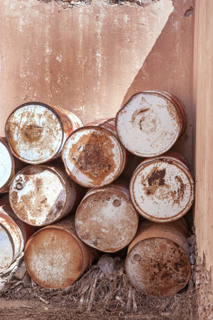 Several, old, rusty barrels were stacked outdoors in the corner of a brown house ruinの写真素材