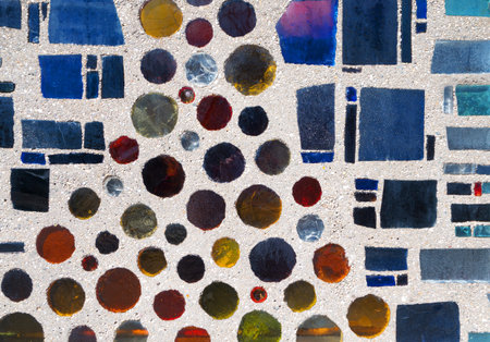Abstract pattern of colorful glass stones with round and square shapes in a gray exterior wall.