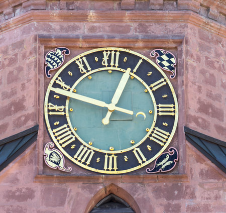 Detail of a round black and golden church clock with roman numerals in a red facade. Taken at the town church in Freudenstadt Germany.の写真素材