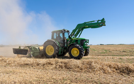 Tractor with straw rake and dust cloud on a stubble field in dry sunny summer