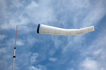 Bright windsock inflated horizontally by the wind, at a thin pole against the skyの写真素材