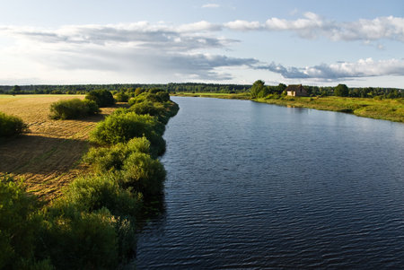 River in rural area with house on the bank under clody skyの写真素材
