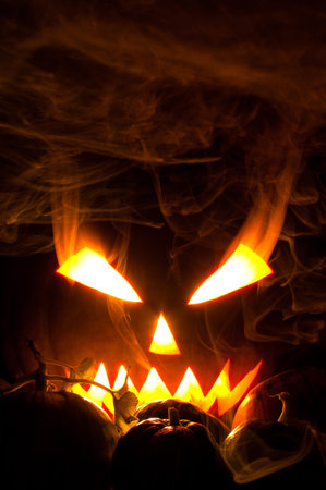 Jack-o-lantern with blazing and smoky eyes in smoke and small pumpkinsの写真素材