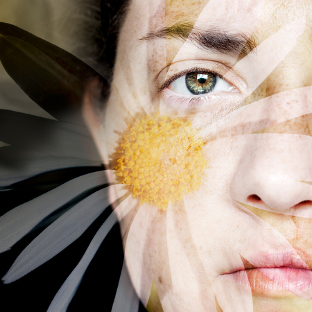 Closeup Artistic Portrait of Woman and with Daisy Superimposed Over Her Face: A double exposure of a woman`s face and a daisy. Only half her face is seen, on the right side of the frame. It is a square crop with a dark background.の写真素材