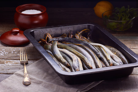 Fresh lamprey ready for cooking in pan, with salt and lemon on wooden tableの写真素材