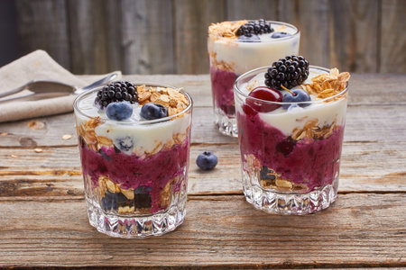 Three yogurt desserts with fresh blueberries, cherries and blackberries on wooden table. Rustic style.の写真素材