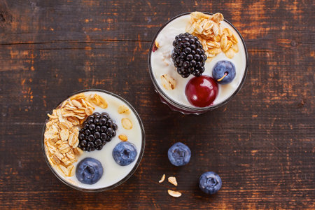 Two yogurt desserts with fresh blueberries, cherries and blackberries on wooden table. Rustic style.の写真素材