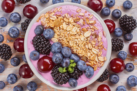 Dish of yogurt smoothie , blackberries, blueberries, cherry and muesli on wooden with berries.の写真素材