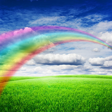 Green field under blue clouds sky with bright rainbow. Beauty nature backgroundの写真素材