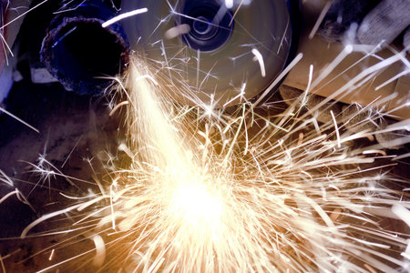 Worker cutting metal using angular grinding machine, orange flying sparks
