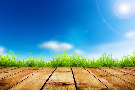 Fresh spring green grass with blue bokeh and sunlight and wood floor  Natural backgroundの写真素材